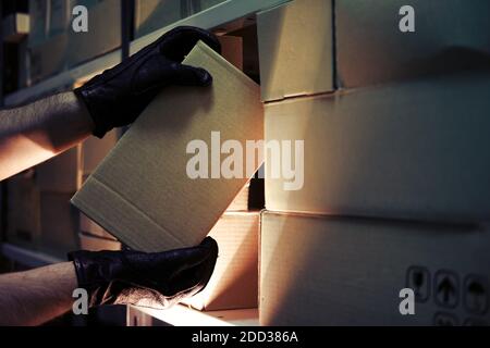 Dieb Hände mit Handschuhen stehlen eine Schachtel Waren in einem Lager in der Dunkelheit. Konzept der Probleme mit Diebstahl von Waren und Postpaketen Stockfoto