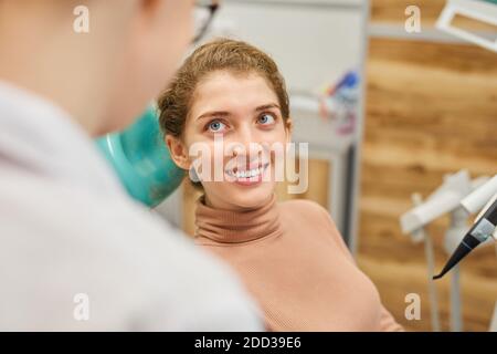 Weibliche Patientin lächelt zum Arzt, während sie auf dem Zahnstuhl sitzt Während des Eingriffs in der Klinik Stockfoto