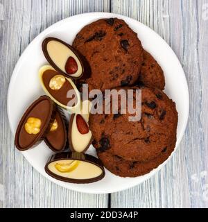 Chocolate Chip Cookies und Schokolade auf einem weißen Teller. Heller Holztisch im provenzalischen Stil. Quadratisches Format Stockfoto