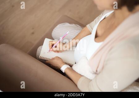 Schwangere Frau macht Notizen. Konzept der Schwangerschaft, Gesundheitsversorgung, Medizin. Mutter wartet auf das Baby zu Hause. Stockfoto