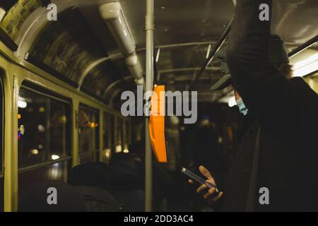 Geschäftsmann pendelt mit der Straßenbahn. Er sieht etwas auf seinem Smartphone, während er steht und sich an der Schiene hält. Stockfoto