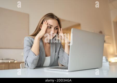 Müde Frau, die mit einem Laptop am Schreibtisch sitzt, den Kopf hält und sich auf der Hand ausruht. Stockfoto