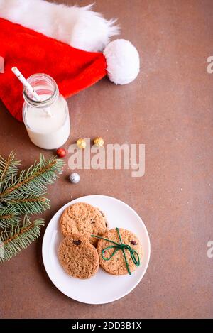 Leckeres Shortbread mit Schokoladenstücken auf einem kleinen Teller, Spielzeug auf dem Weihnachtsbaum, Fichtenspieß, Geschenke, Weihnachtsmütze, Blick von oben. Flach Stockfoto