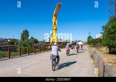 Flussinsel „Ile de Nantes“ (Nordwestfrankreich): Radfahrer im Park „Parc des chantiers“ am Boden des gelben Titan-Krans Stockfoto