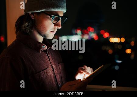 Kaukasischen Geschäftsmann Scrolling auf digitalen Tablet arbeiten spät an Nacht in gemütlicher Wohnung Stockfoto