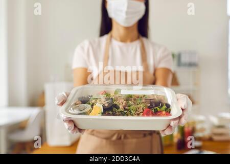 Verantwortungsbewusster Mitarbeiter im Café zum Mitnehmen in der Gesichtsmaske, der das Lunchpaket hält Bereit zur Lieferung Stockfoto