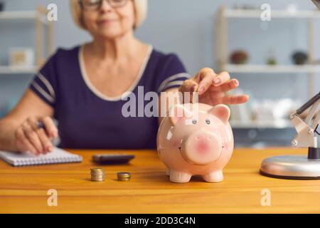 Ältere Frau Frau sitzt mit Geldscheinen und Münzen zu setzen sparschwein zum Sparen Stockfoto