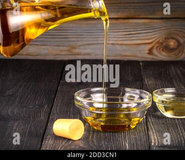 Das Gießen von Speiseöl eine kleine Glastasse auf alt Holztisch Stockfoto