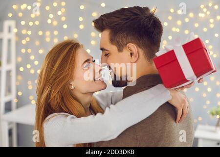 Junge Frau hält Geschenkbox, umarmt ihren Freund und dankt ihm für das Geschenk Stockfoto