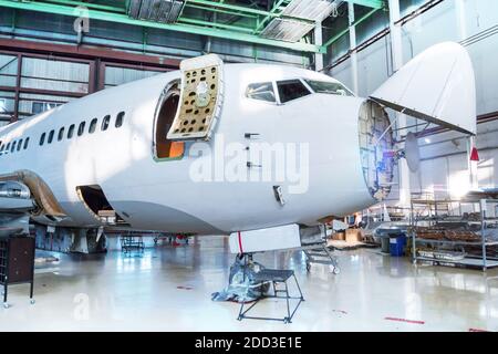 Weißes Passagierflugzeug unter Wartung im Hangar. Mechanische Systeme für Flugbetrieb prüfen. Das Flugzeug hat Wetterradar geöffnet Stockfoto