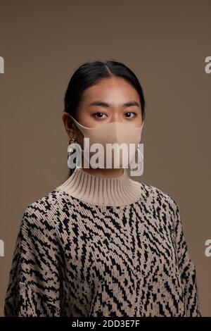 Portrait der asiatischen jungen Frau in Schutzmaske Blick auf Kamera vor dem grauen Hintergrund Stockfoto