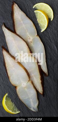 Scheiben gesalzener geräucherter Heilbutt (Steinbutt) auf einem schwarzen Schieferteller. Eine köstliche Fischvorspeise wird mit Zitrone serviert. Meeresfrüchte. Selektiver Fokus Stockfoto