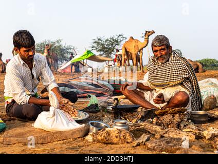 Nomadic rajasthani indischen Mann macht Essen in offener Küche, Töpfe und Pfanne für natürliches Feuer zum Kochen. Stockfoto