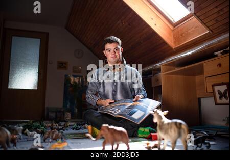 Down-Syndrom erwachsenen Mann mit Haustier Schlange sitzt drinnen im Schlafzimmer zu Hause. Stockfoto