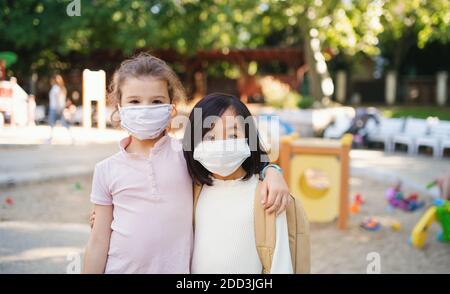 Kleine Schulmädchen mit Gesichtsmaske auf Spielplatz im Freien in der Stadt, Coronavirus Konzept. Stockfoto