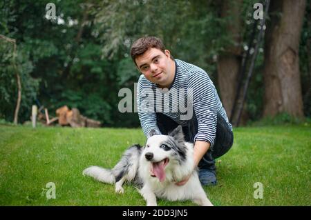 Porträt von fröhlich Down-Syndrom erwachsenen Mann spielt mit Hund im Freien im Hinterhof. Stockfoto