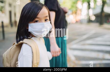 Portrait von kleinen japanischen Mädchen mit Mutter zu Fuß im Freien in der Stadt, Coronavirus Konzept. Stockfoto