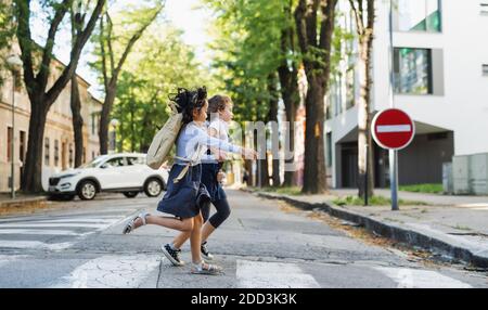 Seitenansicht von kleinen Schulmädchen, die im Freien in der Stadt die Straße überqueren und laufen. Stockfoto