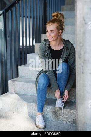 Porträt einer jungen Frau mit roten Haaren im Freien in der Stadt, binden Schnürsenkel auf der Treppe. Stockfoto