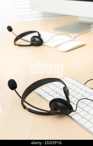Mikrofon-Headsets auf dem Tisch mit Computertastaturen im Callcenter, selektiver Fokus Stockfoto