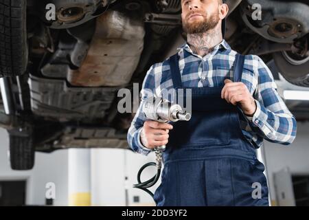 Niedriger Winkel des Technikers, der den Pneumatikschlüssel in der Nähe von oben hält Auto auf unscharfem Hintergrund Stockfoto