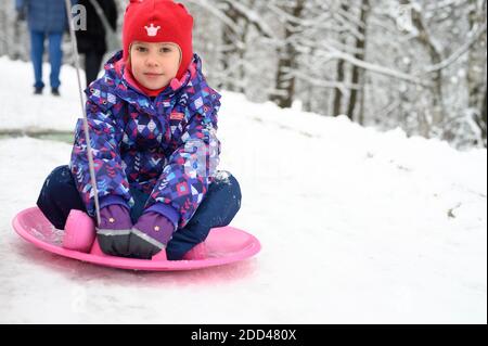 Moskau / Russisch - Januar 2020: Glückliche Familie mit Kindern haben Spaß verbringen Winterferien im verschneiten Winterwald. Kind Mädchen auf Untertasse gleiten Stockfoto