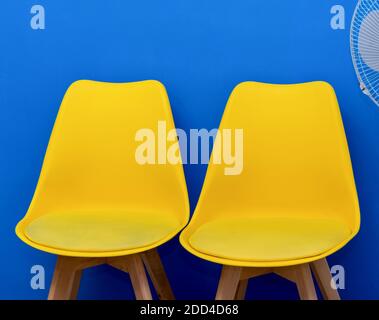 Zwei farbenfrohe gelbe Stühle im Klassenzimmer gegen eine blaue Wand. Nahaufnahme. Minimalistisches Design. Stockfoto