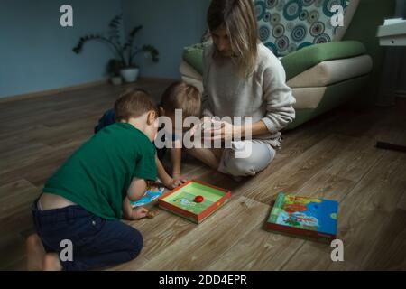 Mutter mit Kindern spielt ein Brettspiel auf dem Boden. Stockfoto