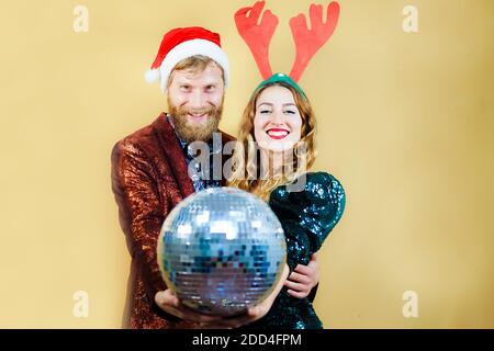 Fröhliche junge elegant gekleidete Paar trägt roten Hut feiern Silvester-Party isoliert auf gelbem Hintergrund. Weihnachten, Neujahr und Party concep Stockfoto