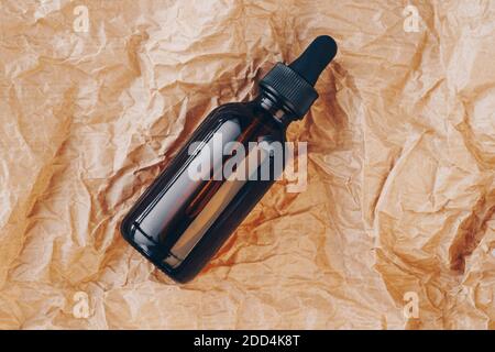 CBD-Ölflasche, Hyaluronsäure-Tinktur auf knittertem Karton. Serum mit Kollagen und Peptiden auf zerknittertem Papier. Modellbau für Schönheitsprodukte Stockfoto