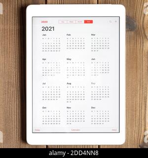 Eine Tablette mit einem offenen Kalender für 2021 Jahr auf einem Holzbrett Tisch Hintergrund. Quadrat Stockfoto