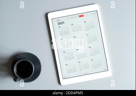 Ein Tablet mit einem offenen Kalender für 2021 Jahre und Eine Tasse Kaffee auf grauem Hintergrund Stockfoto