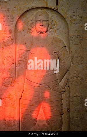 Garitz, Deutschland. November 2020. Das Licht der Sonne scheint durch ein rotes Buntglasfenster auf einen Grabstein, auf dem ein Mitglied von Daviers Familie in Rüstung gekleidet ist. Die Feldsteinkirche aus dem Jahr 1350 wird derzeit mit neuen Fenstern umgestaltet, die alle vom britischen Künstler Tony Cragg entworfen wurden. Quelle: Klaus-Dietmar Gabbert/dpa-Zentralbild/dpa/Alamy Live News Stockfoto