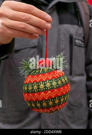 Rot grün gestrickte Weihnachtskugel in der Hand Nahaufnahme. Weihnachten und Neujahr Geschenk, Weihnachtsbaum Spielzeug, Dekoration, Hintergrund Stockfoto