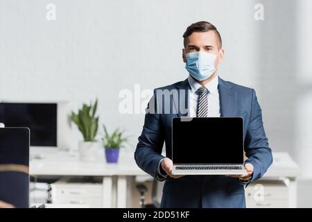 Vorderansicht des Geschäftsmannes mit Laptop mit leerem Bildschirm mit Verschwommenes Büro im Hintergrund Stockfoto