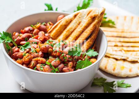 Geschmorte Bohnen in Tomatensauce mit Kräutern und gegrillten Tortillas. Vegetarische gesunde Ernährung Konzept. Stockfoto