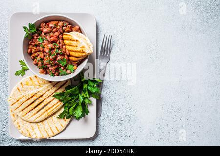 Geschmorte Bohnen in Tomatensauce mit Kräutern und gegrillten Tortillas. Vegetarische gesunde Ernährung Konzept. Stockfoto