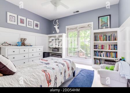 Ein gemütliches Schlafzimmer mit weißen und violetten Wänden, eingebauten Bücherregalen gefüllt mit Büchern und Kinderspielzeug. Stockfoto