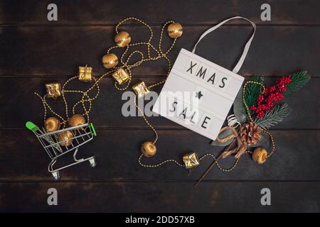 Xmass Sale Wort auf Leuchtkasten und kleinen Warenkorb mit goldenen Geschenken auf Holzhintergrund. Stockfoto