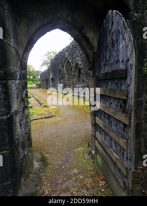 Gewölbtes Tor und Holztür, die zu den Klöstern in Whalley Abbey, Lancashire, Großbritannien 2020 führt) - 1296 zogen die Mönche von Stanlow Point, Cheshire nach Norden nach Whalley, Lancashire, wo sie ein neues Kloster neben dem Fluss Calder bauten. An der Stelle befand sich bereits eine Kapelle, die von Peter von Chester, dem Rektor von Whalley, errichtet wurde, und das Gebäude aus dem 13. Jahrhundert wurde in das neue Kloster integriert. Der Grundstein für die neue Abteikirche wurde im Juni 1296 von Henry de Lacy, dem 10. Baron von Halton, gelegt. Stockfoto