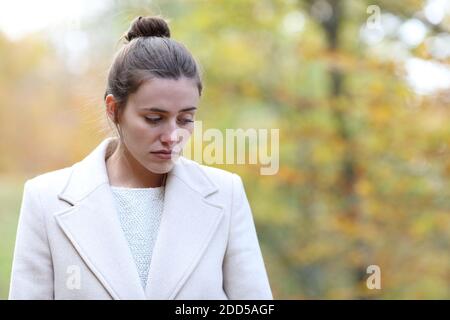 Traurige Frau, die alleine in einem Park hinunterschaut Winter Stockfoto