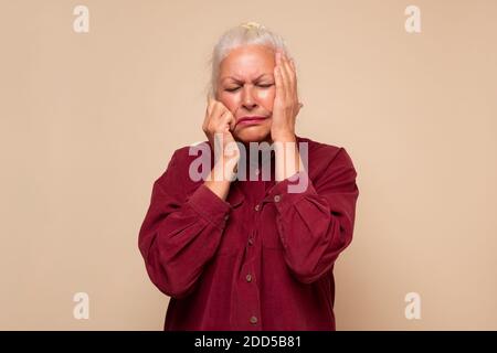 Ältere Frau, die an Kopfschmerzen leidet, verzweifelt und gestresst wegen Schmerzen und Migräne. Studioaufnahme Stockfoto
