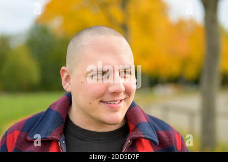 Junger Mann lächelt nachdenklich, während er im Stehen zur Seite schaut Im Freien in einem Herbstpark aus nächster Nähe Stockfoto