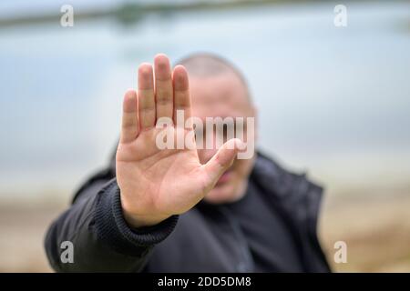 Der Mensch, der mit der Hand eine Stop- oder Stop-Geste macht Halten Sie die Handfläche an die Kamera, wobei der Fokus auf seine gerichtet ist Hand im Freien an einem Strand Stockfoto