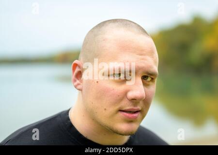 Unrasiert junger Mann in einem Nahaufnahme Kopf Porträt suchen An der Seite des Rahmens mit ruhigen See Hintergrund Stockfoto