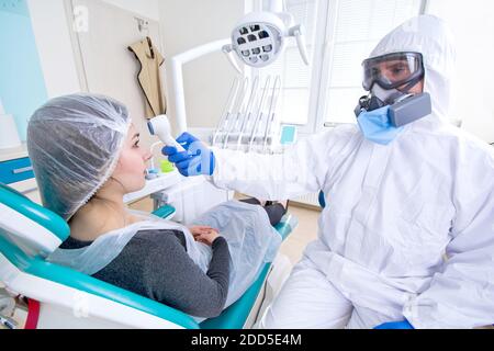 Arzt in Schutzanzug Uniform und Maske Kontrolle der Temperatur der jungen weiblichen Patienten. Ausbruch des Coronavirus. Covid-19-Konzept. Stockfoto