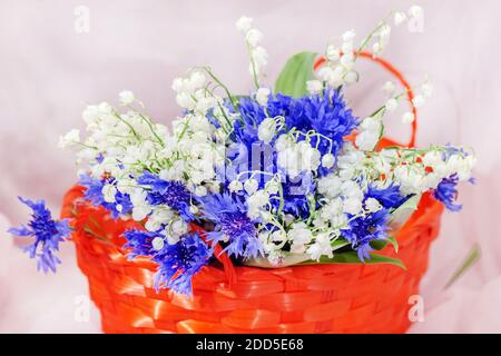 Hübsche Frühlingslilien des Tales und Kornblumen in Orange Korb Stockfoto
