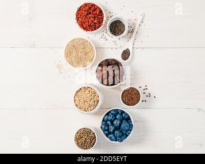 Verschiedene superfoods in kleinen Schüssel auf weiße Holztisch. Auswahl super Essen. SUPERFOOD wie Heidelbeeren, Chia, rohen Kakaobohne, Goji, Hanf samen, Quinoa, brauner Reis. Platz für Text kopieren. Top View oder flach Stockfoto