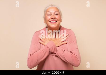 Ältere Frau immer Komplimente frisch aussehen. Entzückte glücklich charmante alte Dame mit weißen Haaren hält Palmen auf Herz Stockfoto