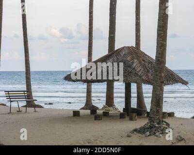 Silhouette Bild von einem strohgedeckten Schatten mit einer Bank zu Sitzen Sie an einem Strand in Port Blair in Andaman und Nicobar-Inseln Indien Stockfoto